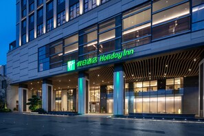 Un hôtel moderne doté d’une entrée imposante, de grandes fenêtres et d’une façade bien éclairée.