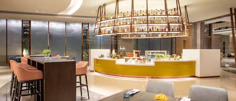 A modern hotel lobby with a central bar area, seating arrangements, and a decorative ceiling light fixture.