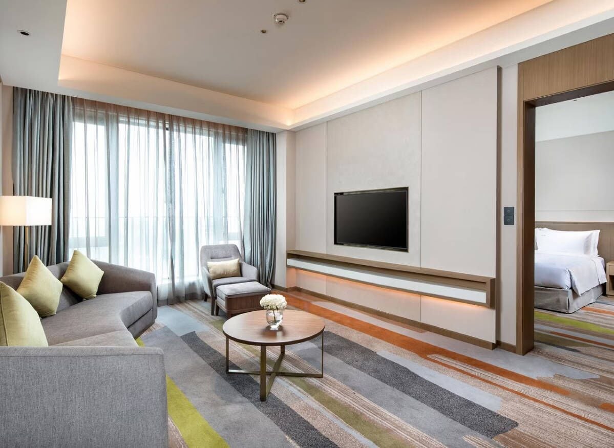 A hotel room with a sofa, armchair, TV, and a bed.