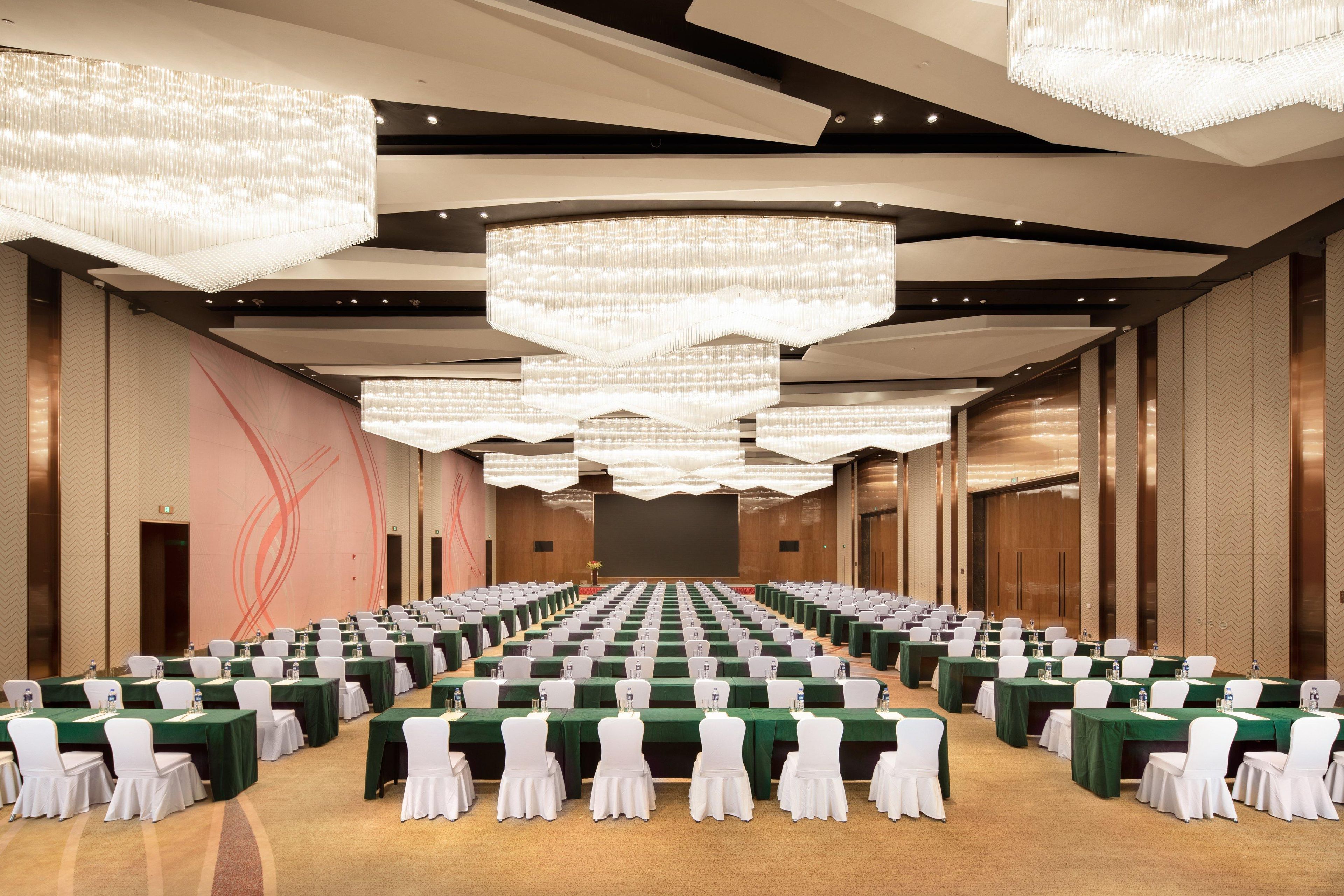 A conference room with rows of tables, chairs, and large chandeliers.