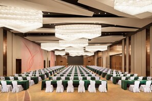 Une salle de conférence avec des rangées de tables, des chaises et de grands lustres.
