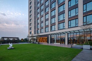 A modern building with a glass facade, a well-maintained lawn, and a clear sky. - Holiday Inn Foshan Shunde (Foshan)