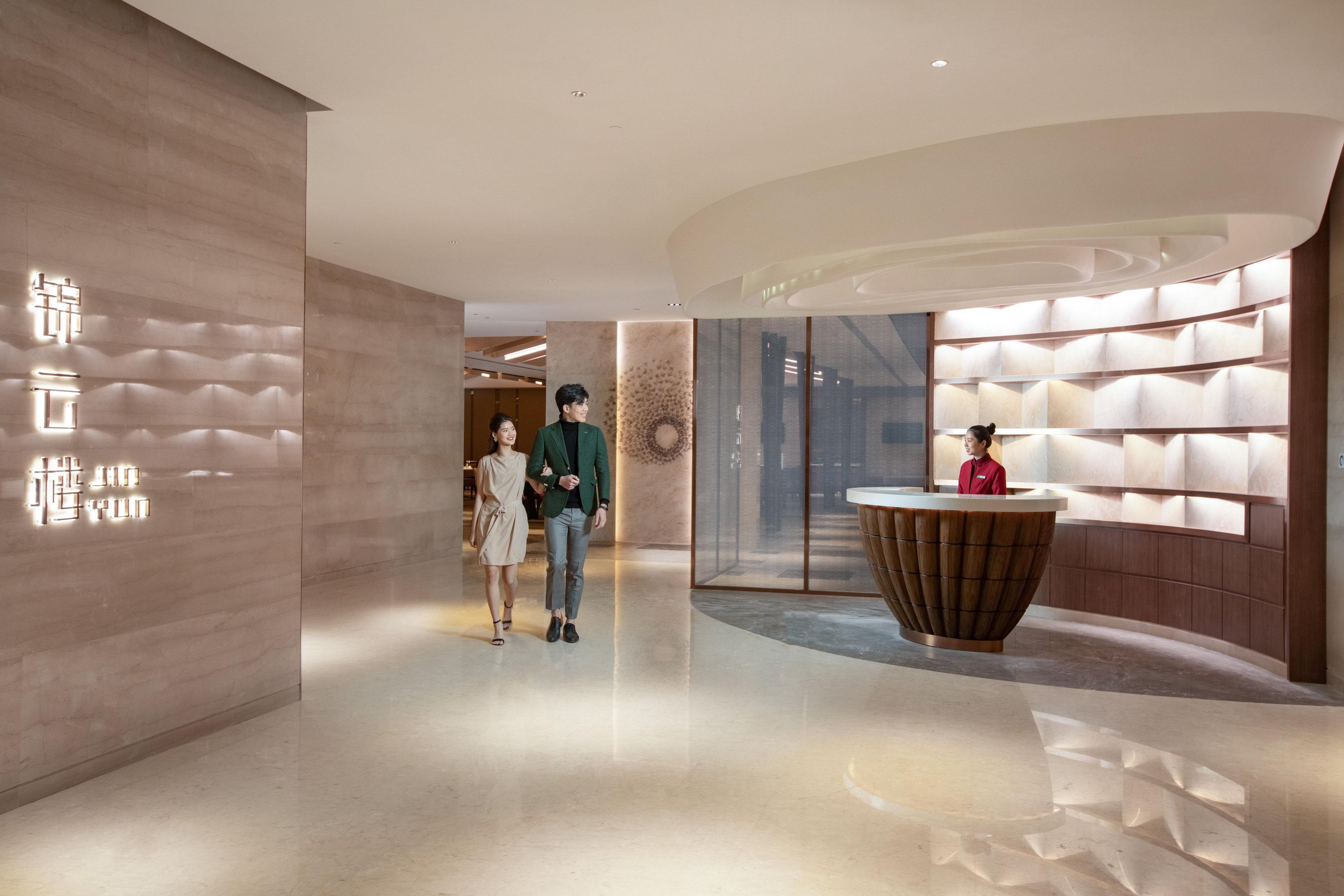 Una hall d'hotel moderna con una reception, una parete decorata con un motivo geometrico e un pavimento lucido.