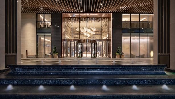Entrada de hotel moderna com porta giratória, fachada de vidro e acesso em níveis.