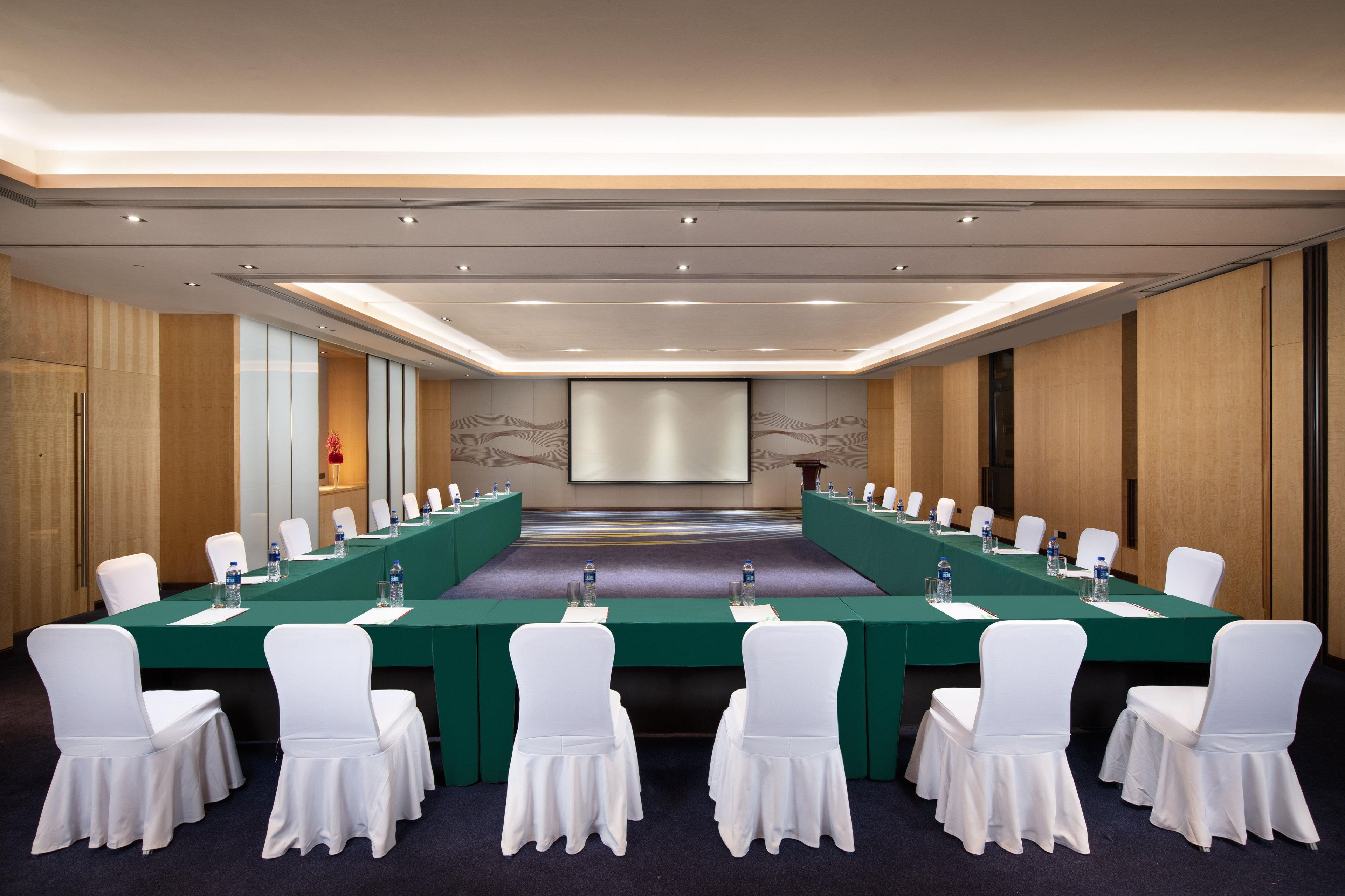 Une salle de conférence avec une longue table, des chaises blanches et un écran de projection.