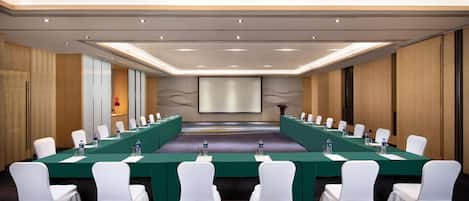A conference room with a long table, white chairs, and a projector screen.