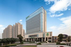 A modern hotel with a glass facade, a covered entrance, and a landscaped courtyard. - Holiday Inn Foshan Shunde (Foshan)