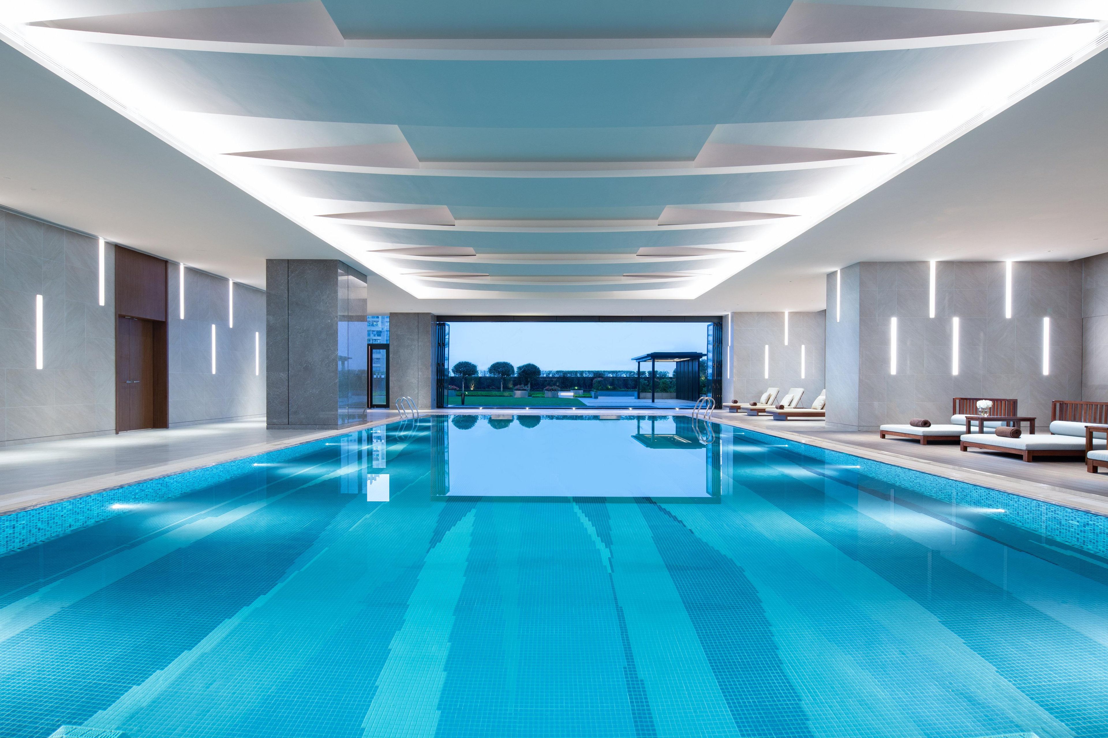 En moderne indendørs swimmingpool med krystalklart udsyn til himlen og et loungeområde ved poolen.