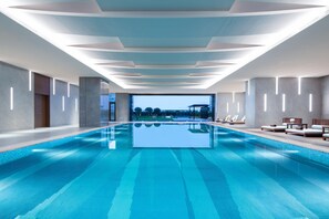 Une piscine intérieure moderne offrant une vue dégagée sur le ciel et dotée d’un espace de détente au bord de la piscine.