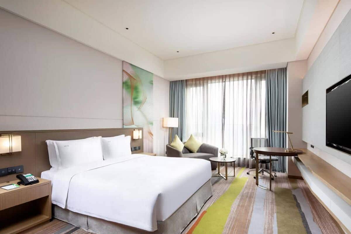 A hotel room with a large bed, a desk with a phone, a chair, a small table, and a TV.
