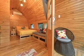A cozy wooden cabin bedroom with a bed, a wicker chair, and a small window. - CoCo Farm Hoi An (Da Nang)