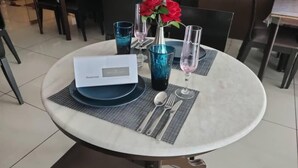 Une table de salle à manger ronde, avec un set de table blanc, une pancarte indiquant qu’elle est réservée et un vase rempli de fleurs rouges.