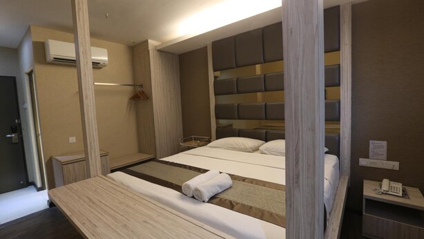 Une chambre d’hôtel moderne avec un grand lit, une tête de lit en bois et une table de chevet avec un téléphone.