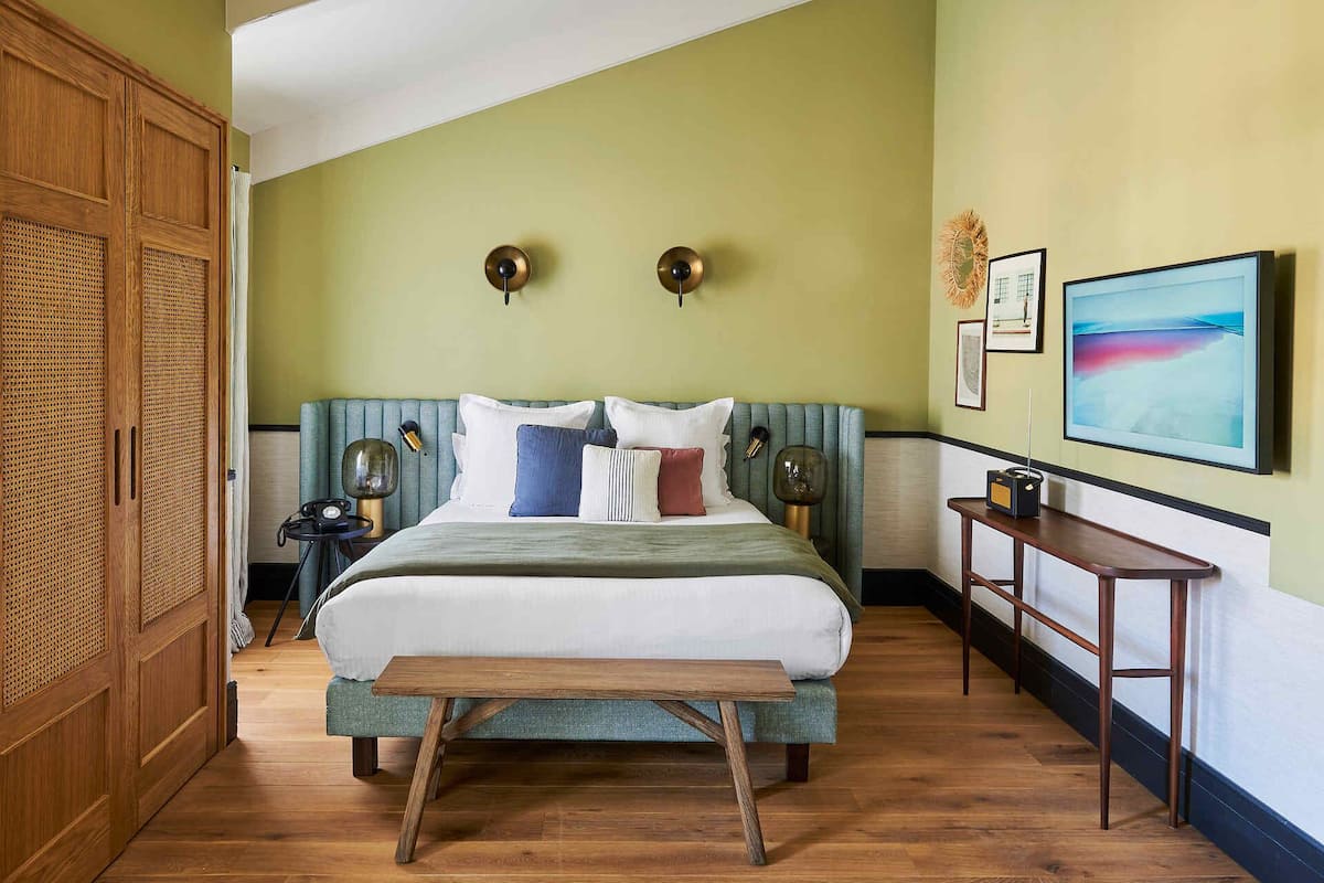 A bedroom with a bed, bedside tables, a bench, a wall-mounted TV, and artwork.