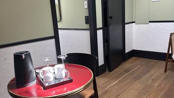 A room with a dining table set with a coffee maker, glasses, and a tray. There are two chairs, a door, and a wall-mounted light fixture.