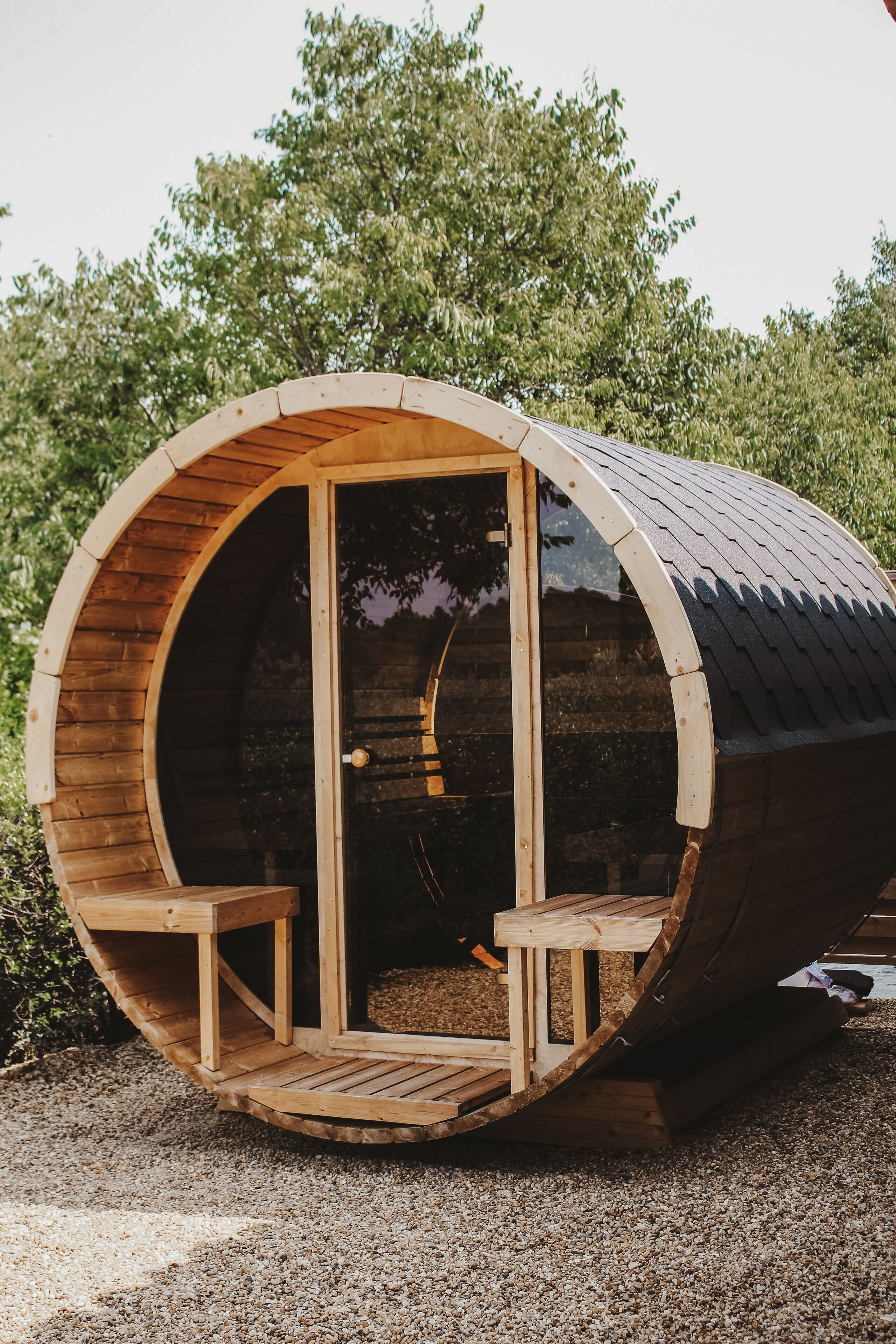 Une structure en bois en forme de tonneau, dotée d’une porte et de deux bancs à l’intérieur.
