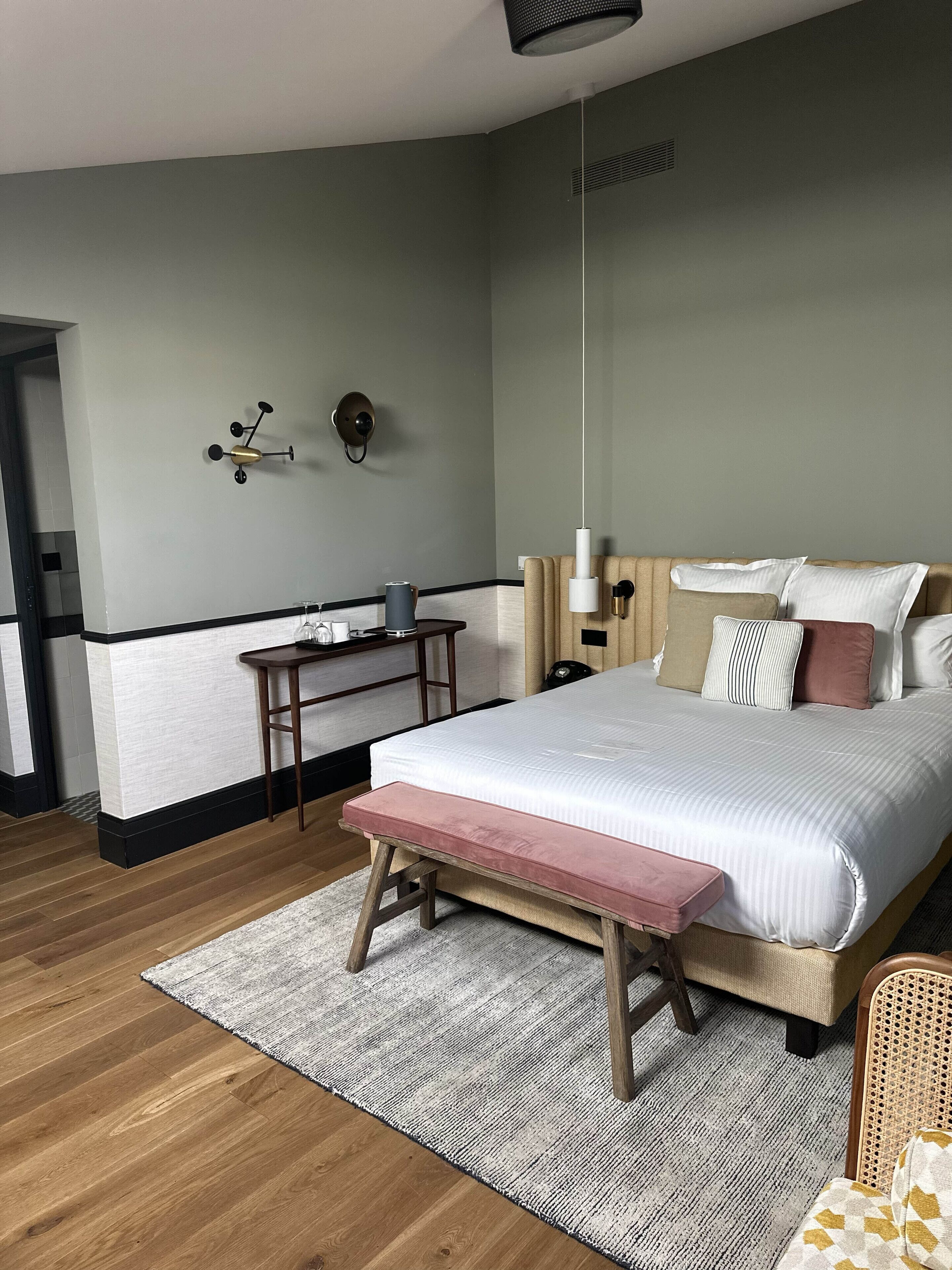 A modern bedroom with a bed, bedside table, lamp, and a small desk with a chair.