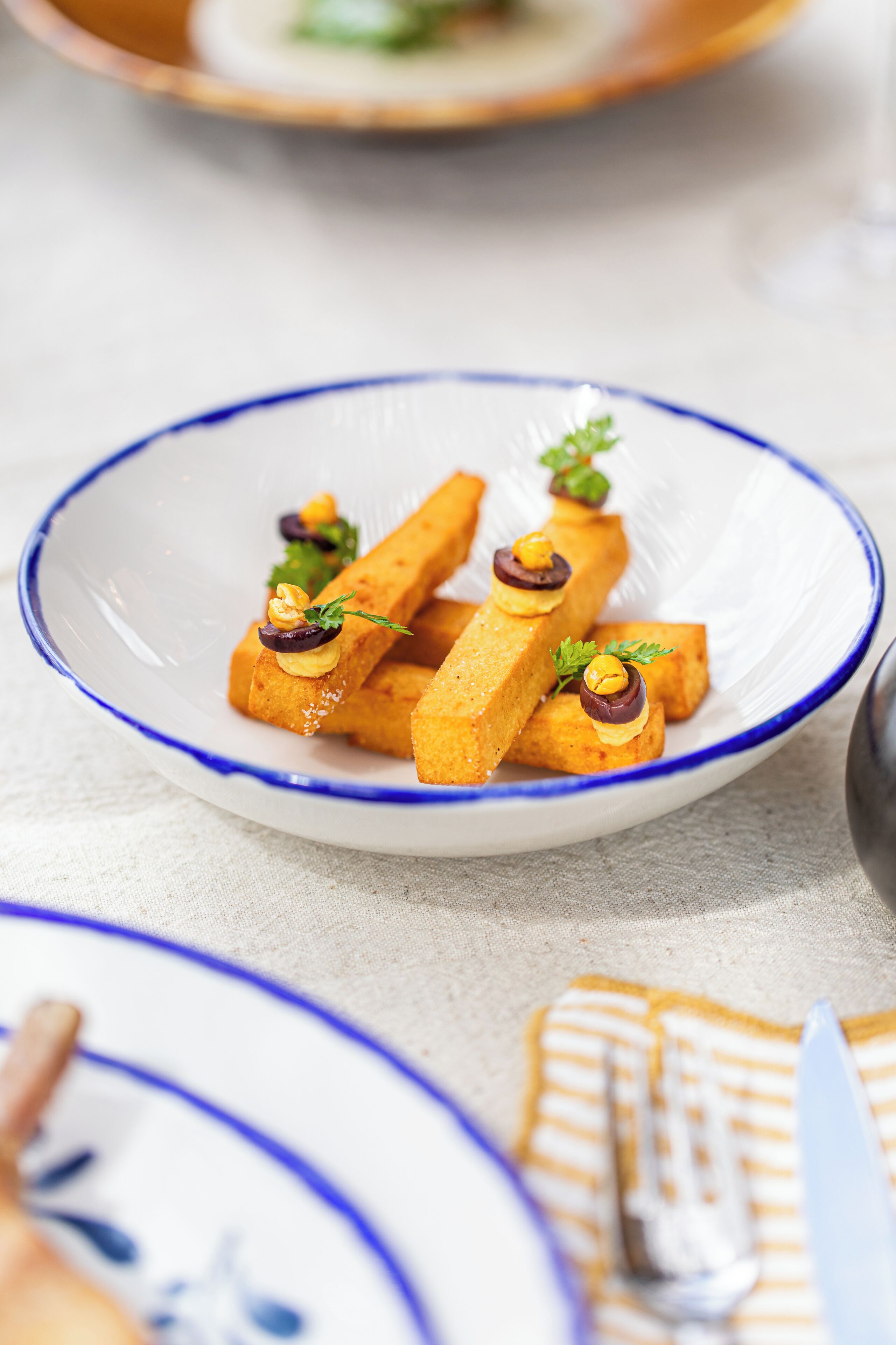 A white plate with blue rim containing rectangular food items garnished with herbs and nuts.