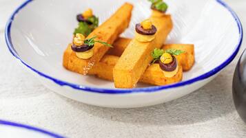 A white plate with blue rim containing rectangular food items garnished with herbs and nuts.