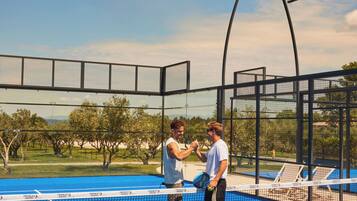 Cancha de tenis con red, dos jugadores y una pelota.