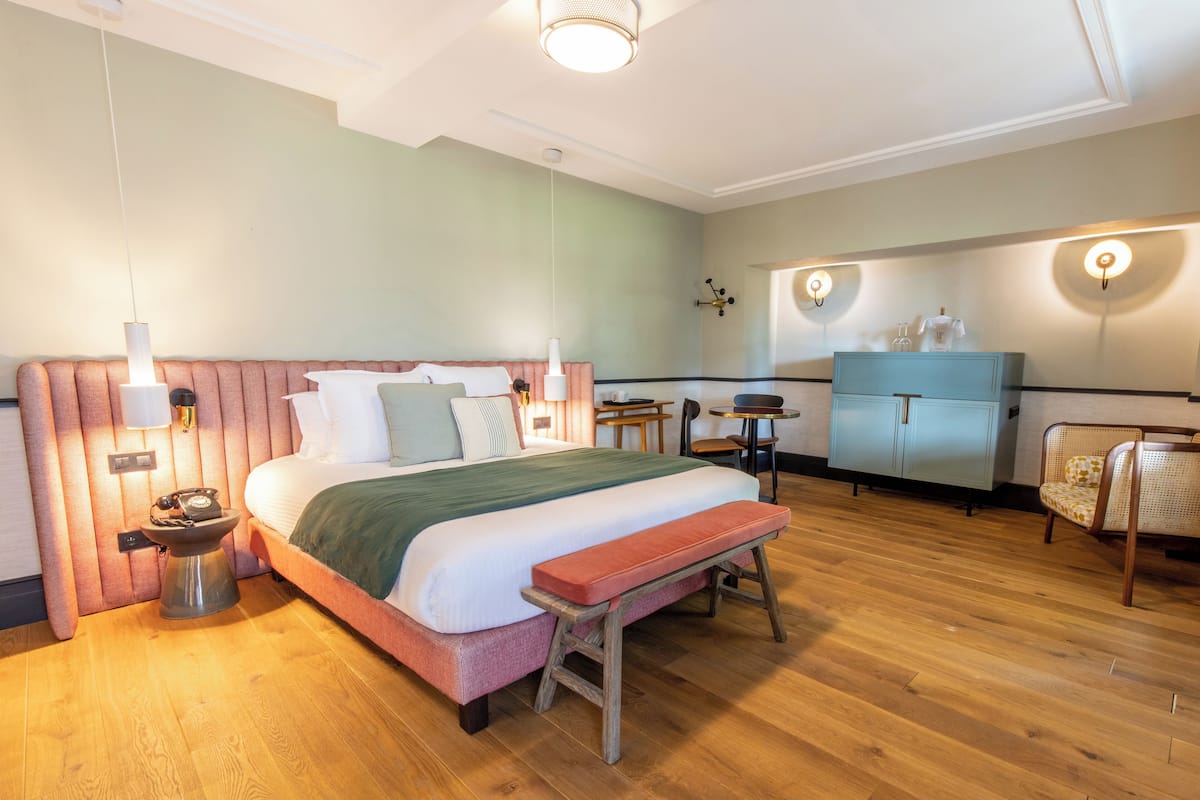 A hotel room with a large bed, a wooden bench, a desk, and a wardrobe.