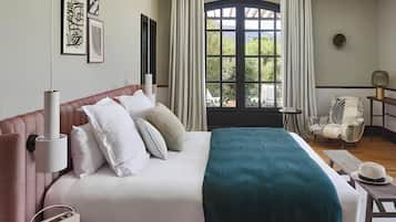 A hotel room with a bed, a window with curtains, a chair, and a lamp.