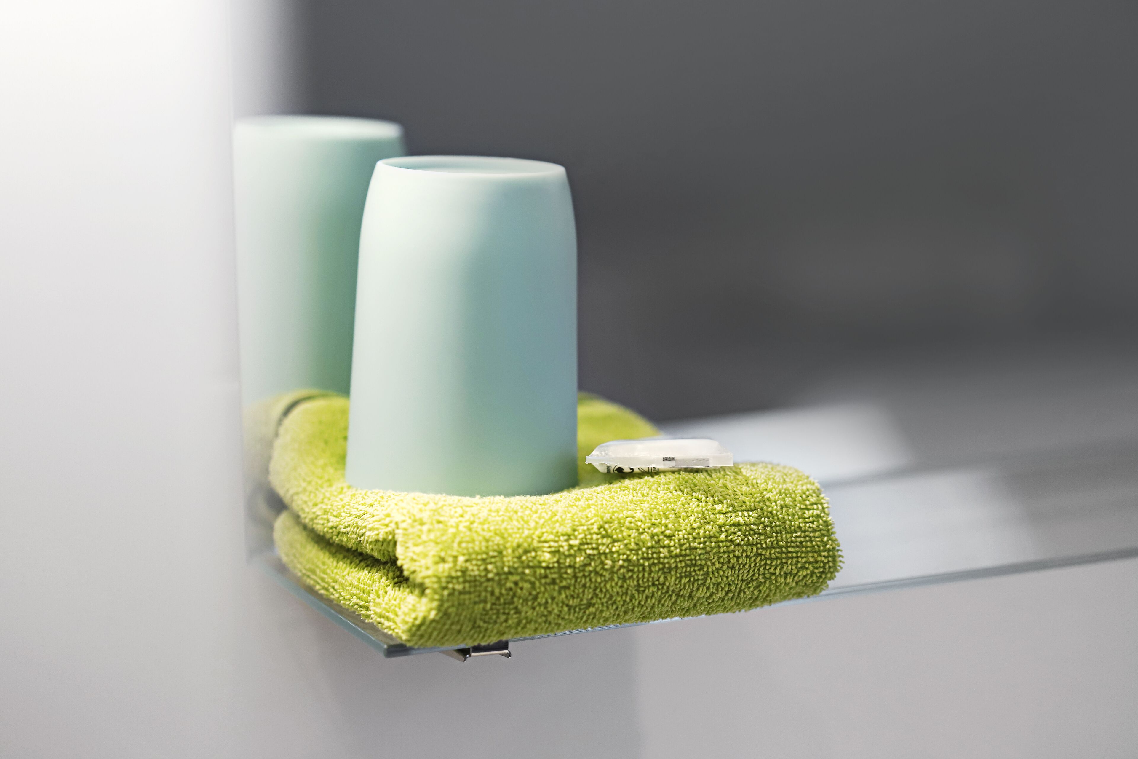 Two cylindrical objects on a shelf, a green towel, and a small electronic device.