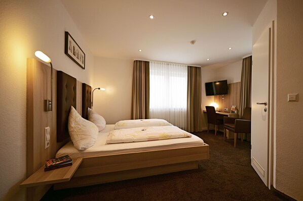 A hotel room with a bed, bedside table, desk, chair, and a television.