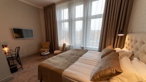 A hotel room with a large bed, a TV mounted on the wall, a desk with a chair, and a window with curtains. - Orsa Järnvägshotell (Orsa)
