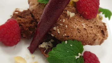 A dessert with chocolate mousse, raspberries, mint leaves, and a decorative element.