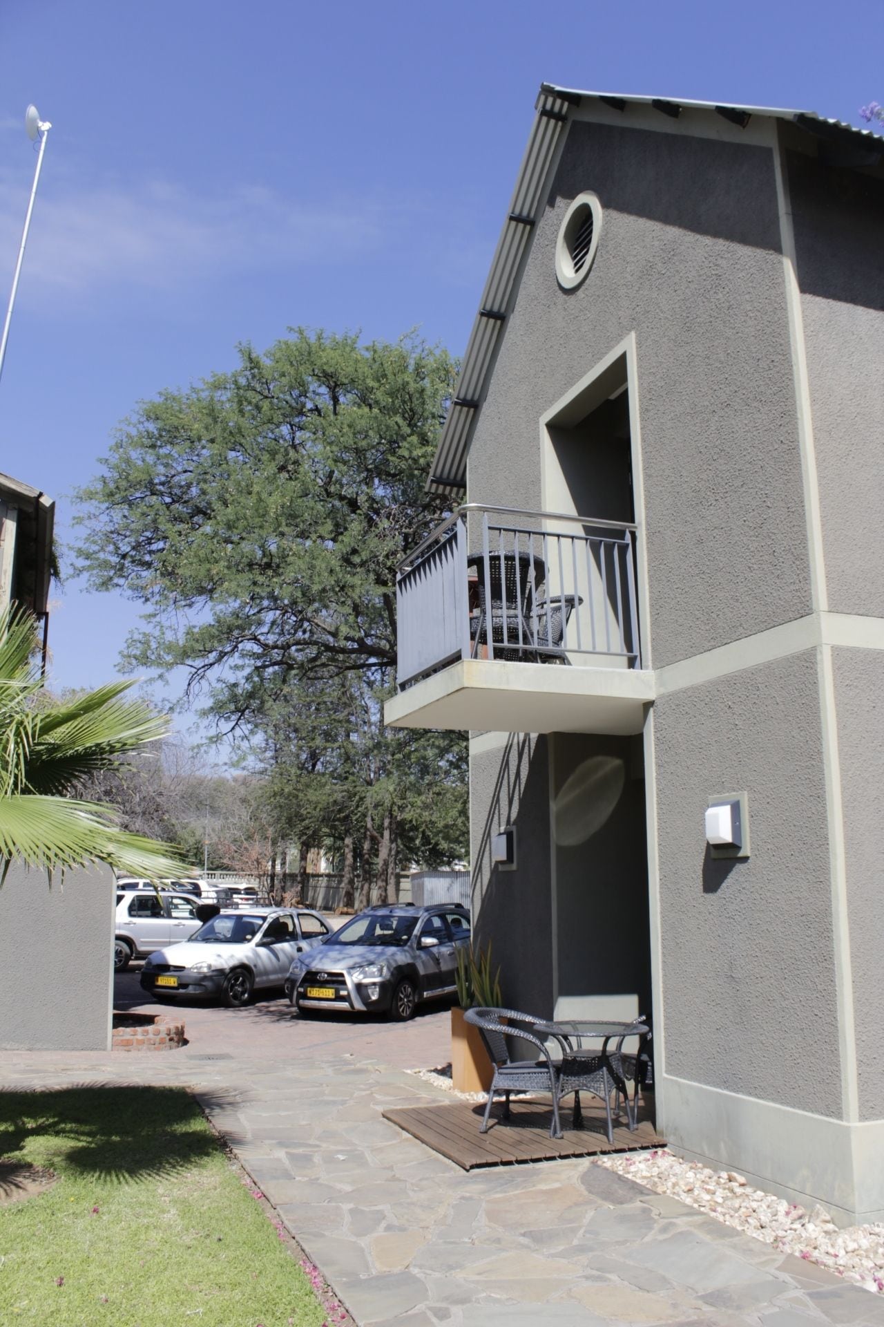 A two-story building with a balcony, a staircase, and a parking area with cars.