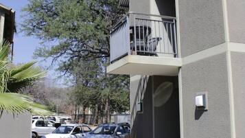 A two-story building with a balcony, a staircase, and a parking area with cars.