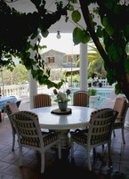Una mesa redonda con seis sillas a rayas, una planta en maceta y vistas de una casa y piscina.