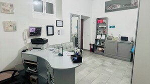 A modern office space with a central desk, computer, printer, and a small seating area. - Grandis Rooms (Rome)