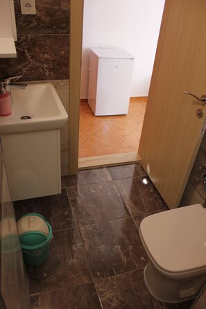 Un baño con lavamanos, inodoro y un armario blanco. Hay dos cubos verdes en el suelo.