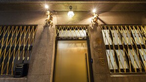 Entrada de un edificio con una reja metálica, una puerta con manija y una lámpara arriba.