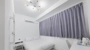 Un dormitorio moderno con una cama blanca, una mesita de noche, un escritorio con silla, un ventanal con cortinas y una lámpara de techo.