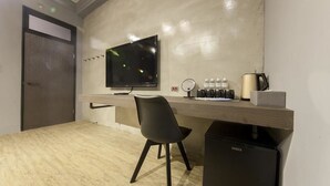 Un espacio de oficina moderno con una televisión de pantalla plana, un escritorio, una silla, una máquina de café y un refrigerador pequeño.