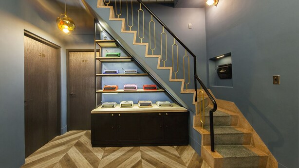 Una escalera con detalles de madera, una barandilla negra y varios estantes que exhiben máquinas de escribir antiguas.