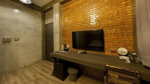 Un baño con pared de ladrillo, televisor de pantalla plana, lavamanos y espejo.