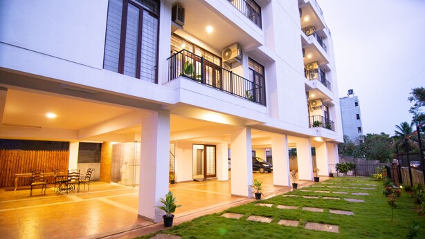 A multi-story residential building with a covered patio area, outdoor seating, and a well-maintained garden. - Stay At (Bengaluru)