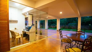 A modern kitchen with a glass partition, a dining area with a round table and chairs, and a view of the outdoors. - Stay At (Bengaluru)