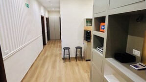 A hallway with striped walls, a wooden floor, and a kitchenette area with stools and a small fridge.