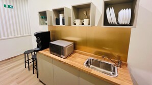 A modern kitchen with a built-in microwave, a stainless steel sink, and storage shelves for cups and dishes.