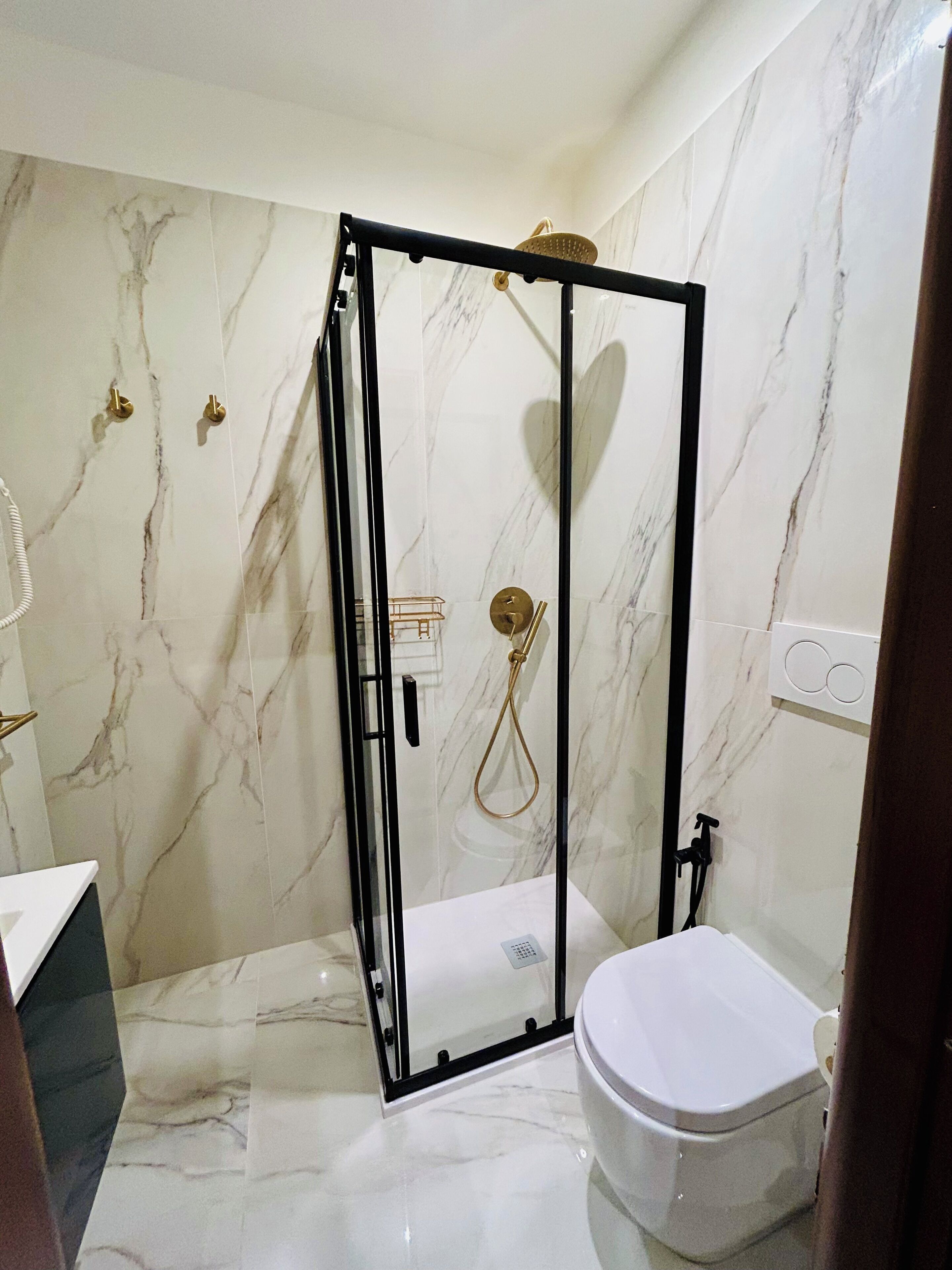 A modern bathroom with a glass-enclosed shower, a toilet, and marble walls.
