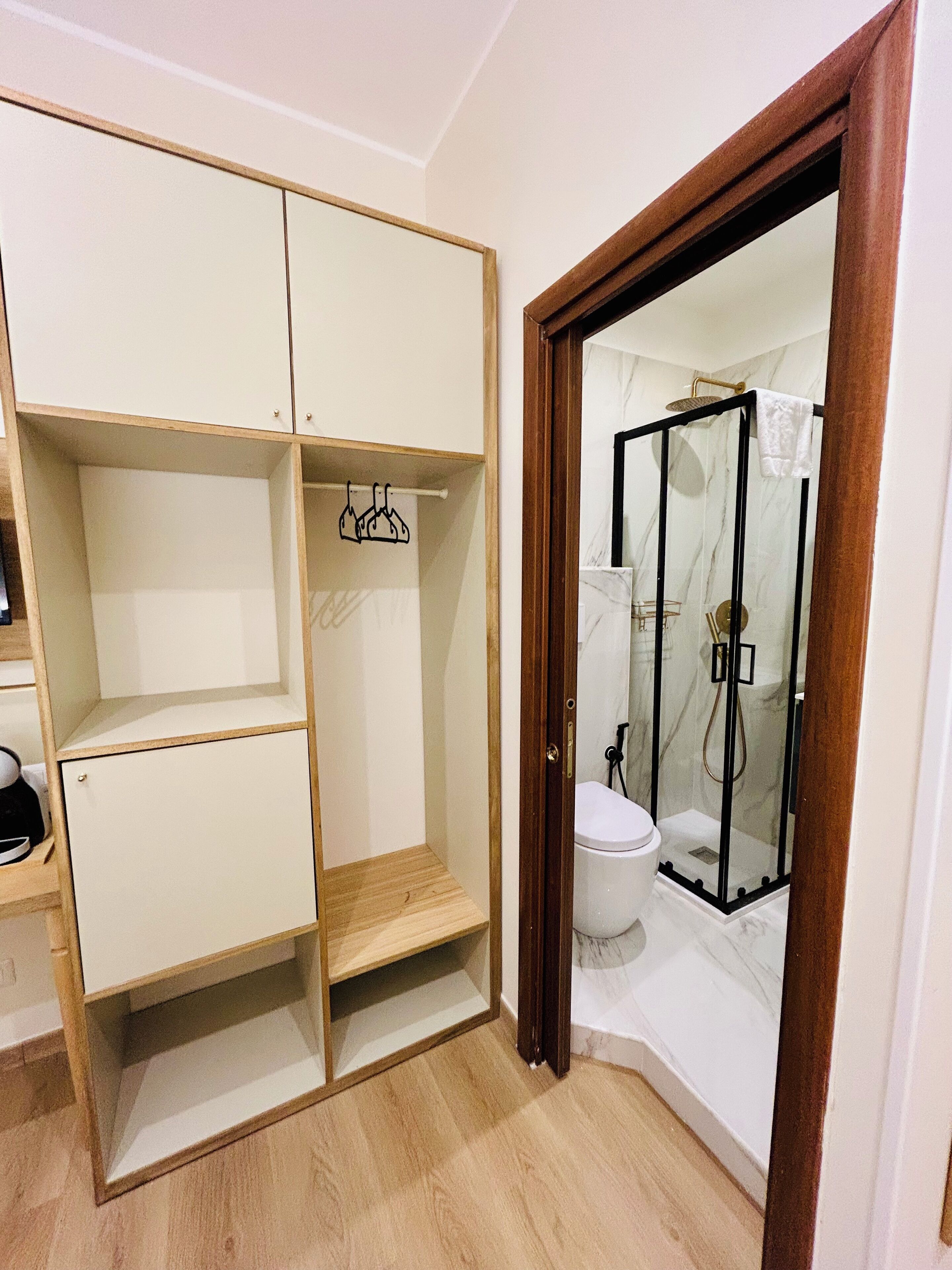 A compact bathroom with a shower enclosure, a toilet, and a storage unit with shelves.