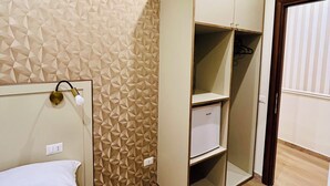 A bedroom with a bed, a wardrobe, a wall with geometric pattern, and an air conditioning unit.