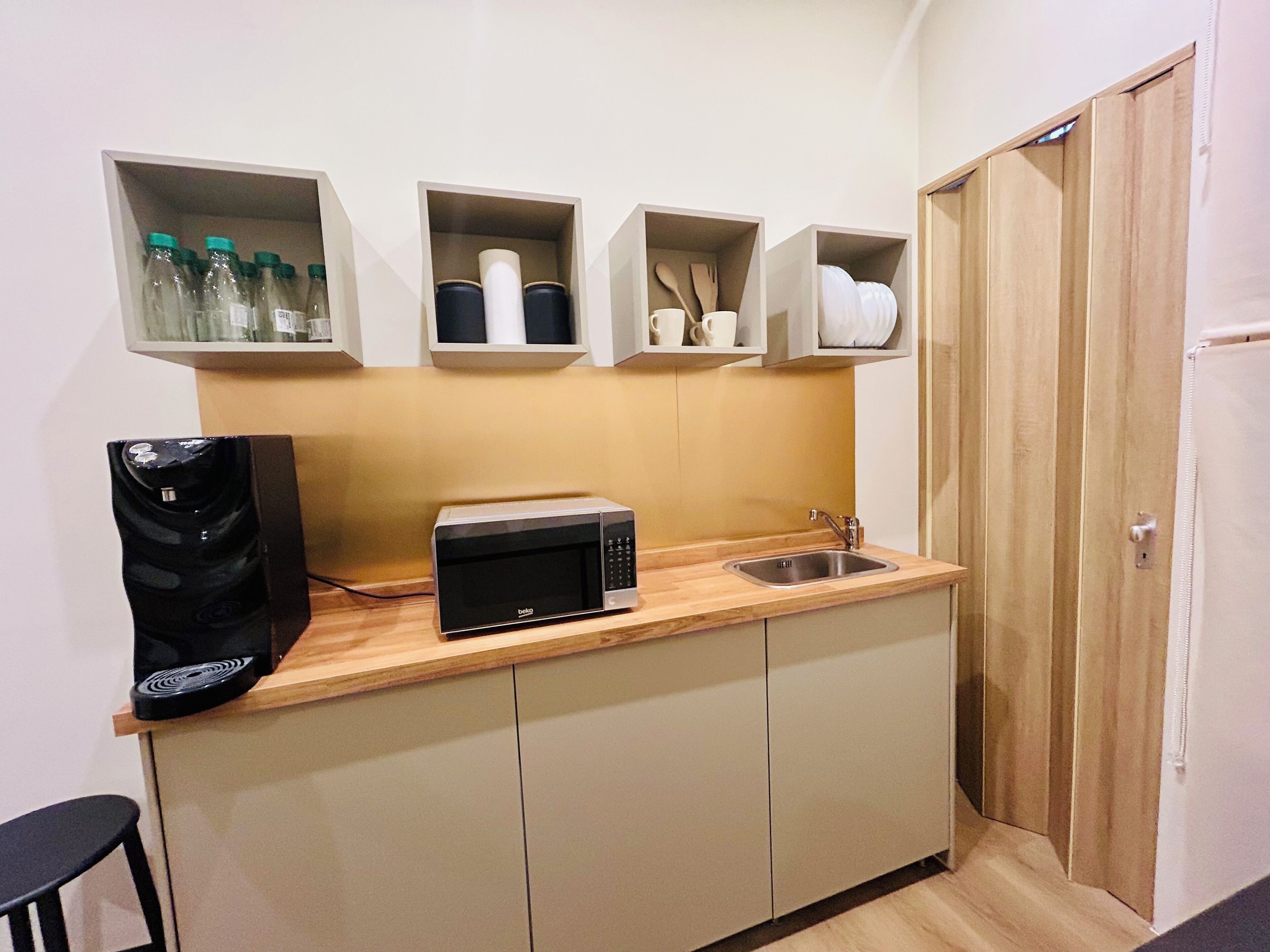 A compact kitchenette with a microwave, a coffee maker, and shelves above containing bottles and kitchenware.