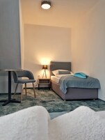 Ein Schlafzimmer mit Bett, Schreibtisch, Stuhl, Nachttisch mit Lampe und Deckenleuchte.