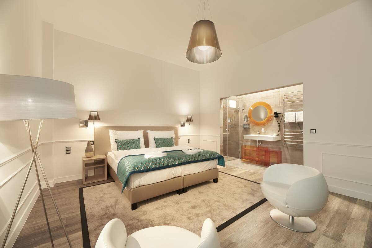 A modern bedroom with a bed, bedside tables, a chair, and a bathroom with a mirror and sink.